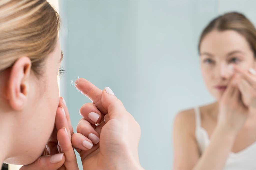 Woman looking in the mirror putting in a contact lens (MODEL)