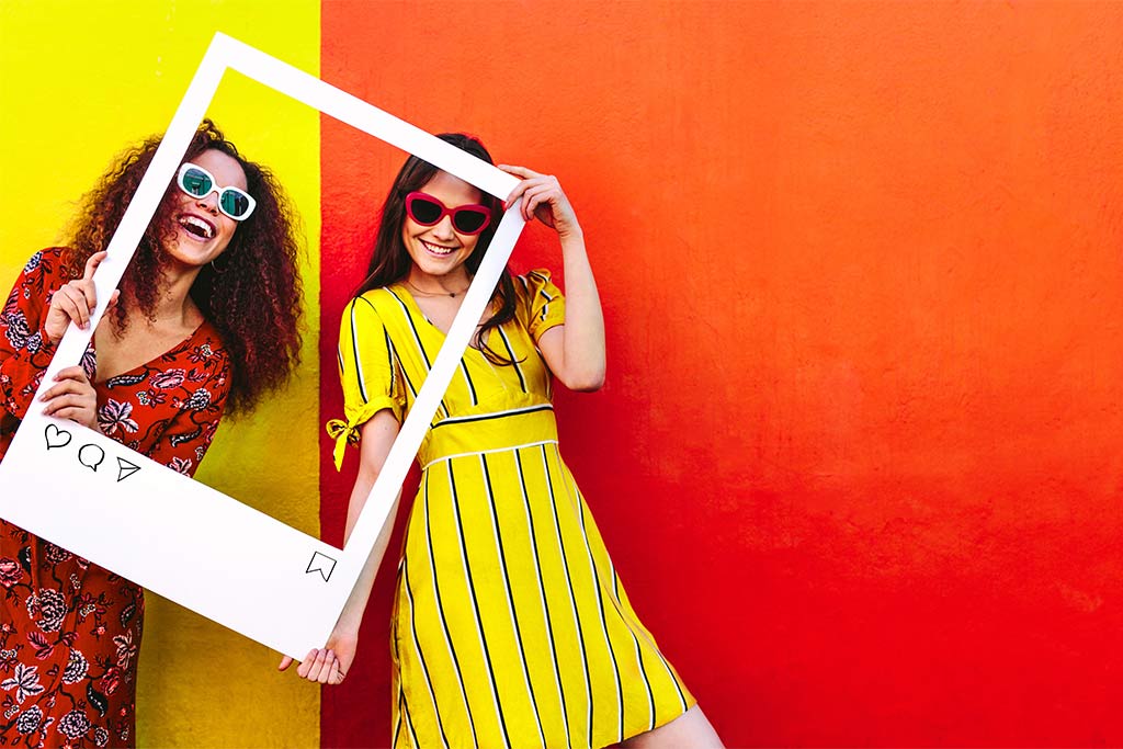 nJoy Vision Summertime is LASIK Time blog post feature image of two young woman posing for a photo with a photo frame prop