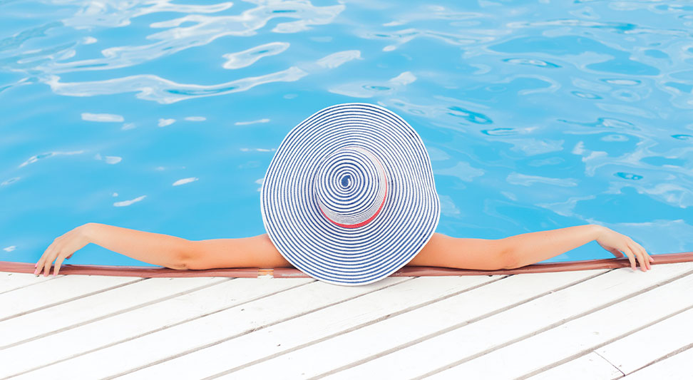 nJoy Vision Summertime is LASIK blog post story image of a woman in a sunhat relaxing at the edge of a pool