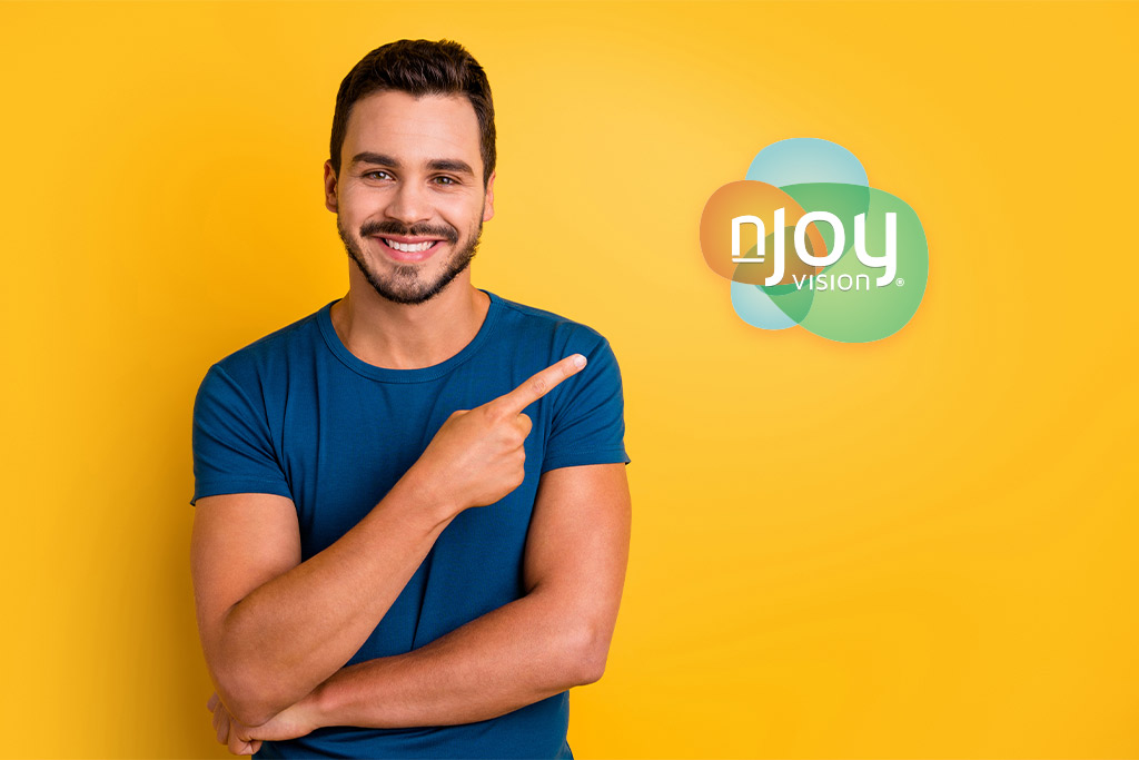 nJoy Vision Visian ICL and LASIK Alternatives blog post feature image of a smiling young man standing against a yellow-orange backdrop pointing over his shoulder to the nJoy Vision logo